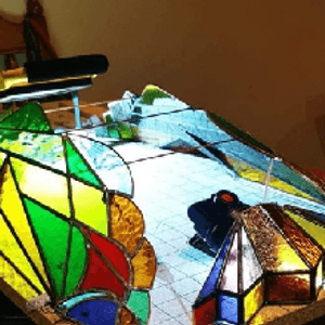Green, yellow, red and blue stained glass peices sitting on a paper design on a desk