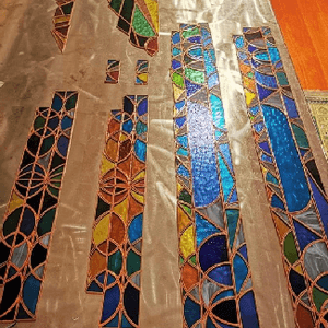 Brightly coloured stained glass strips lying on a plastic sheet on a wooden floor